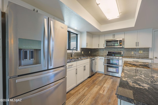 kitchen with dark stone counters, stainless steel appliances, sink, white cabinets, and light hardwood / wood-style floors