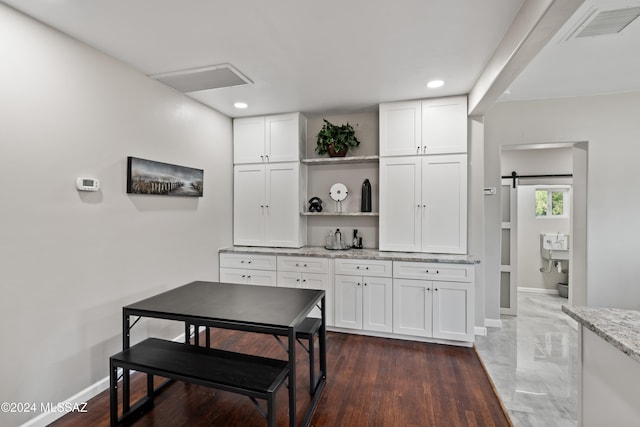 kitchen featuring white cabinetry, a barn door, and light stone counters