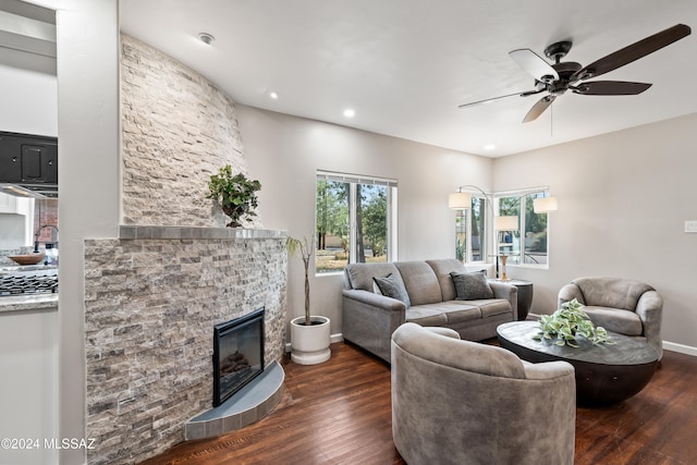 living room with dark wood-type flooring, ceiling fan, plenty of natural light, and a stone fireplace