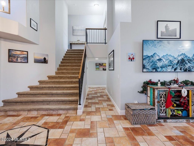 stairs with stone finish flooring, a high ceiling, and baseboards