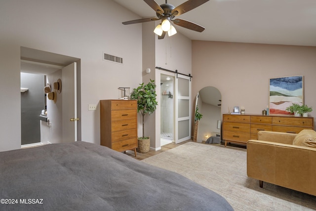 bedroom with connected bathroom, a barn door, ceiling fan, and high vaulted ceiling