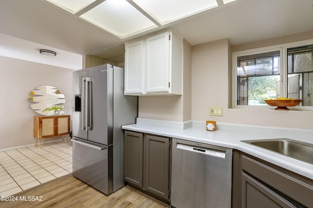 kitchen with gray cabinetry, sink, stainless steel appliances, white cabinets, and light wood-type flooring