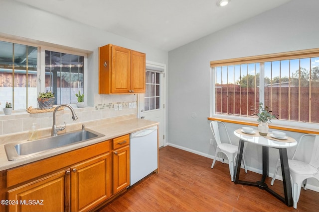 kitchen featuring tasteful backsplash, white dishwasher, vaulted ceiling, sink, and light hardwood / wood-style floors