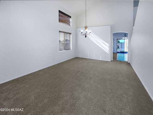 unfurnished living room with a notable chandelier, a wealth of natural light, carpet, and high vaulted ceiling