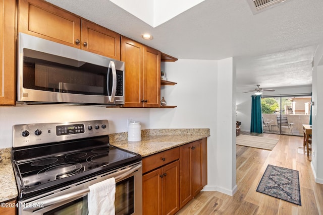 kitchen with light stone countertops, light hardwood / wood-style flooring, a textured ceiling, and appliances with stainless steel finishes