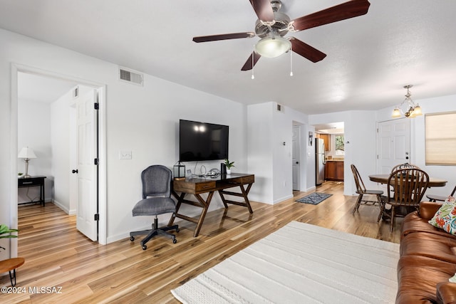 living room featuring ceiling fan with notable chandelier and light wood-type flooring