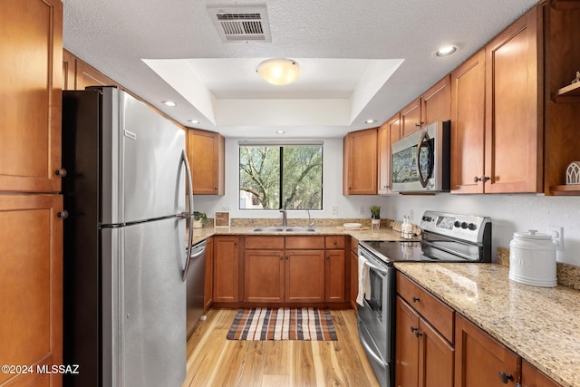 kitchen featuring light stone countertops, appliances with stainless steel finishes, a raised ceiling, sink, and light hardwood / wood-style floors