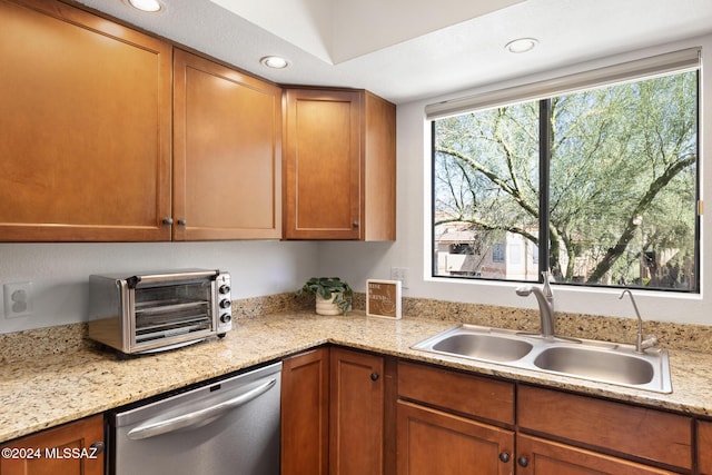 kitchen featuring stainless steel dishwasher, light stone counters, and sink