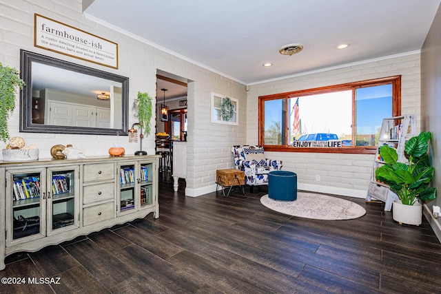 living area with crown molding, hardwood / wood-style floors, and brick wall