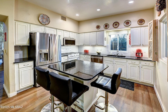 kitchen with appliances with stainless steel finishes, sink, light hardwood / wood-style floors, white cabinetry, and a breakfast bar area