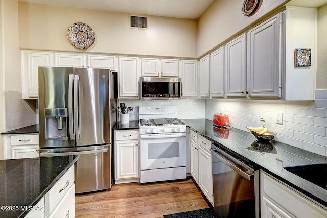 kitchen with light wood-type flooring, tasteful backsplash, dark stone counters, stainless steel appliances, and white cabinets