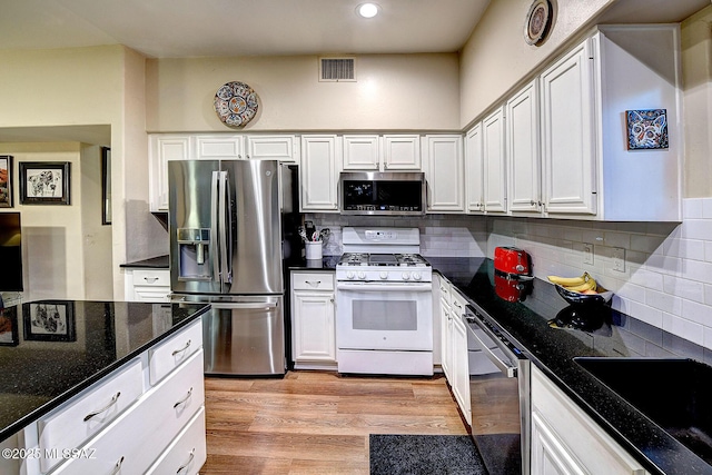 kitchen featuring dark stone counters, light hardwood / wood-style flooring, appliances with stainless steel finishes, tasteful backsplash, and white cabinetry