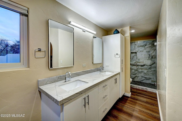 bathroom with a tile shower, vanity, and wood-type flooring