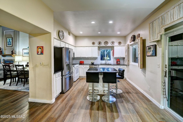 kitchen with stainless steel refrigerator with ice dispenser, a kitchen breakfast bar, white range with gas stovetop, a center island, and white cabinetry