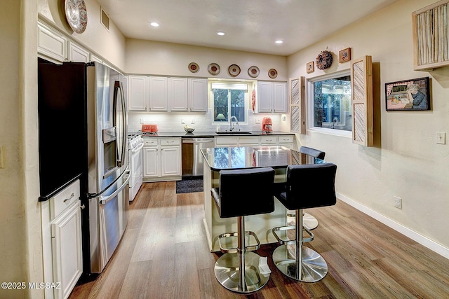 kitchen with backsplash, white cabinetry, a breakfast bar, and appliances with stainless steel finishes