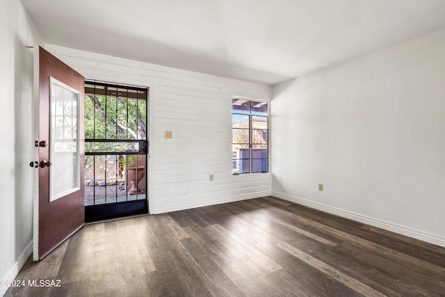 spare room featuring dark hardwood / wood-style flooring, plenty of natural light, and brick wall