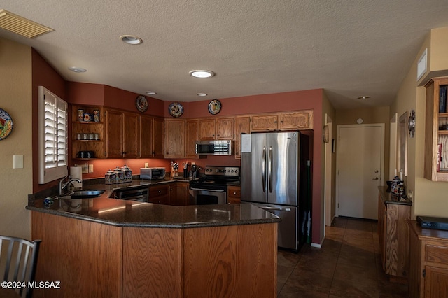 kitchen featuring kitchen peninsula, appliances with stainless steel finishes, a textured ceiling, dark tile patterned floors, and sink