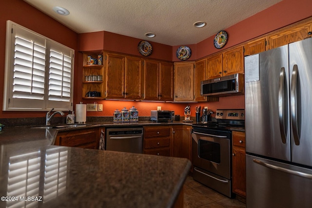 kitchen with appliances with stainless steel finishes, a textured ceiling, dark tile patterned floors, and sink