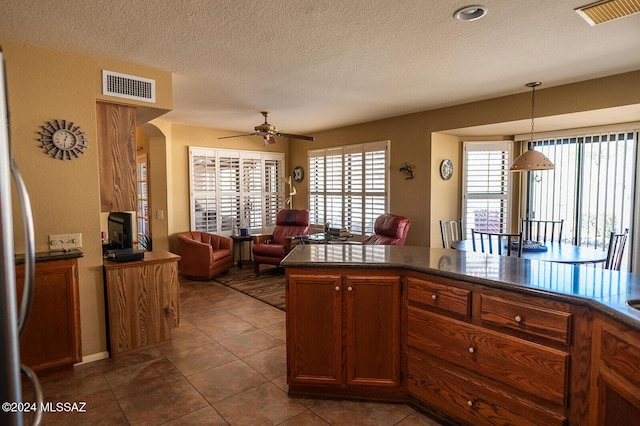 kitchen featuring ceiling fan, stainless steel fridge, a textured ceiling, decorative light fixtures, and dark tile patterned flooring