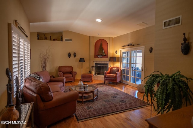 living room featuring hardwood / wood-style flooring, a tile fireplace, and vaulted ceiling