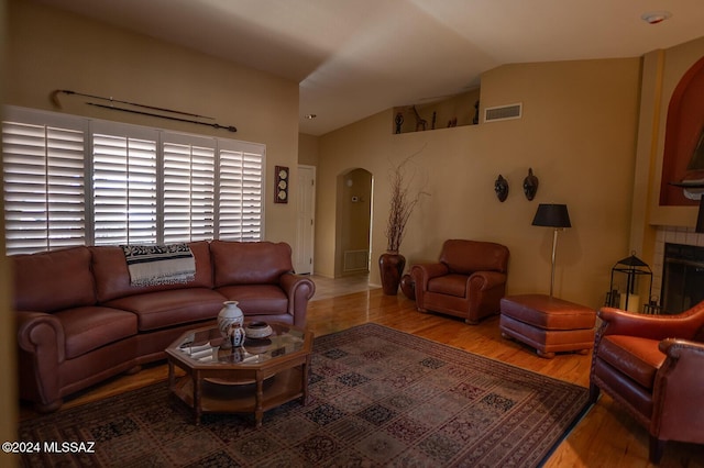 living room with hardwood / wood-style flooring, lofted ceiling, and a tile fireplace