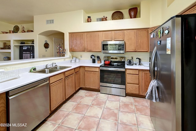 kitchen with kitchen peninsula, light tile patterned floors, sink, and appliances with stainless steel finishes