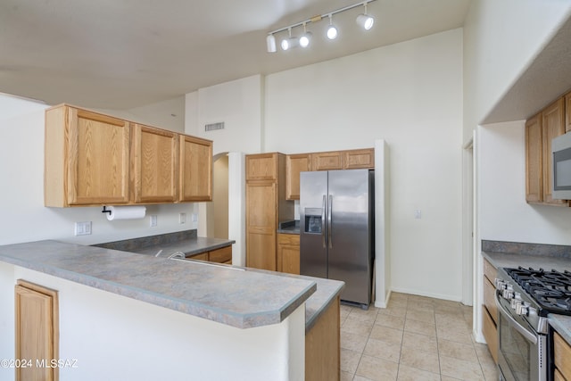 kitchen featuring kitchen peninsula, light tile patterned floors, a high ceiling, and appliances with stainless steel finishes