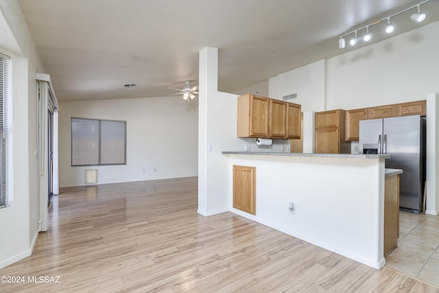 kitchen featuring ceiling fan, kitchen peninsula, stainless steel fridge, vaulted ceiling, and light wood-type flooring