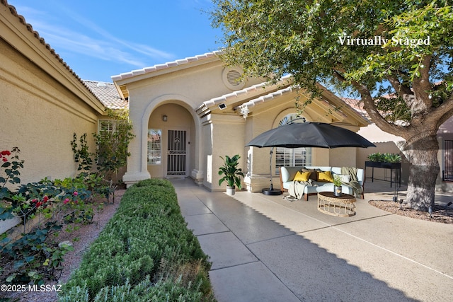 view of exterior entry with stucco siding, a tiled roof, and a patio