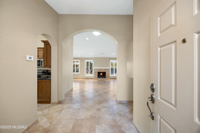 entrance foyer with arched walkways, baseboards, recessed lighting, a tile fireplace, and light tile patterned floors