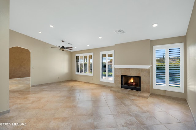 unfurnished living room featuring visible vents, a ceiling fan, light tile patterned flooring, arched walkways, and a tiled fireplace