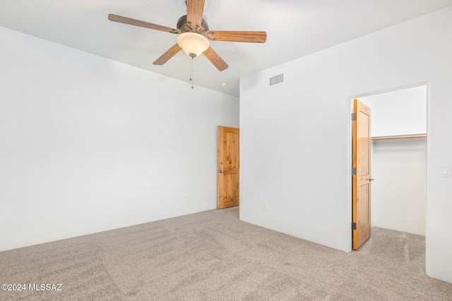 unfurnished bedroom featuring ceiling fan, a walk in closet, light carpet, and a closet