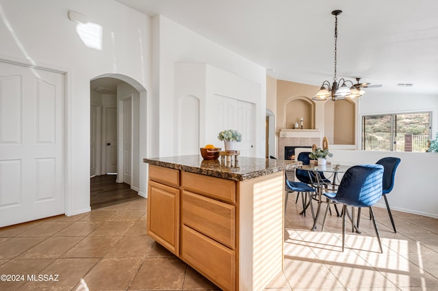 kitchen featuring a center island, hanging light fixtures, a notable chandelier, dark stone counters, and a tiled fireplace