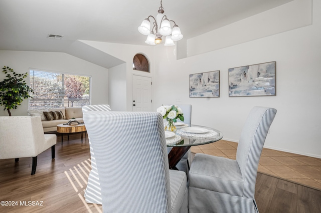 dining area with hardwood / wood-style floors, lofted ceiling, and an inviting chandelier