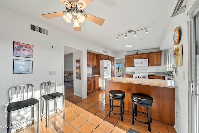 kitchen with ceiling fan, kitchen peninsula, white appliances, a breakfast bar, and light tile patterned floors