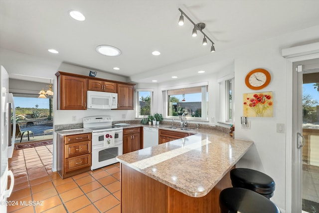 kitchen featuring white appliances, sink, light tile patterned floors, light stone counters, and kitchen peninsula