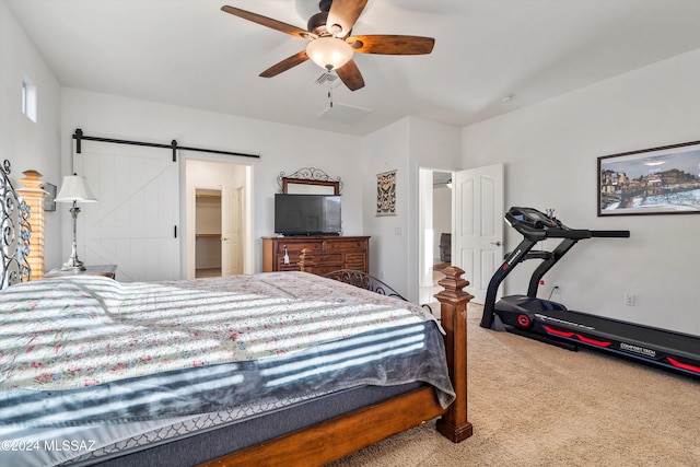 bedroom with carpet, a walk in closet, ceiling fan, a barn door, and a closet