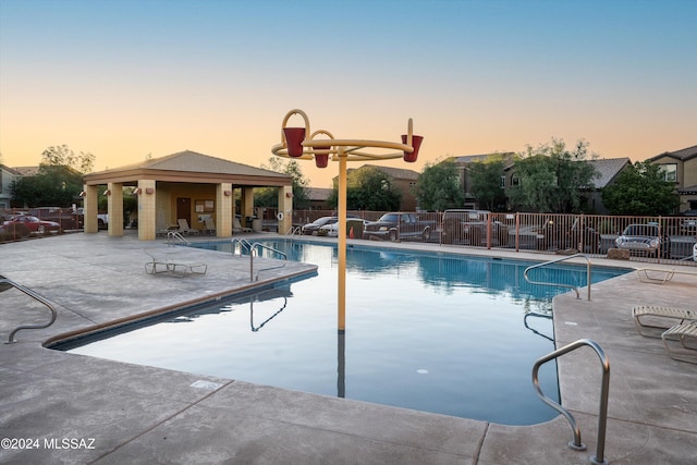 pool at dusk featuring a gazebo and a patio