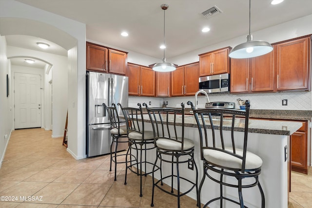 kitchen with stainless steel appliances, an island with sink, pendant lighting, a breakfast bar, and light tile patterned floors