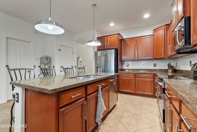 kitchen with sink, stainless steel appliances, an island with sink, decorative light fixtures, and a breakfast bar area