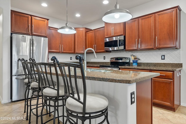 kitchen with a center island with sink, decorative light fixtures, a breakfast bar, and appliances with stainless steel finishes