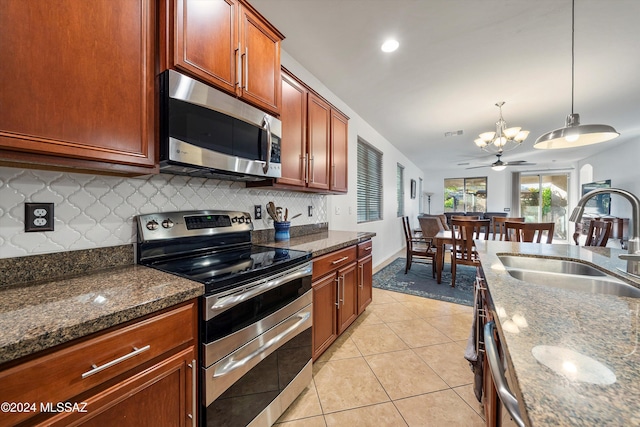 kitchen with sink, stainless steel appliances, dark stone countertops, pendant lighting, and ceiling fan with notable chandelier