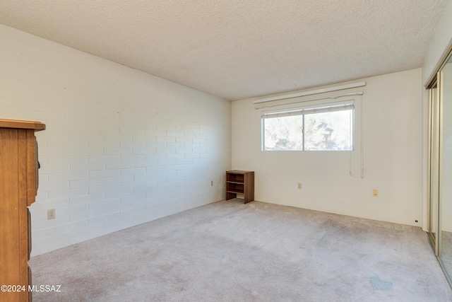 carpeted empty room with a textured ceiling and brick wall