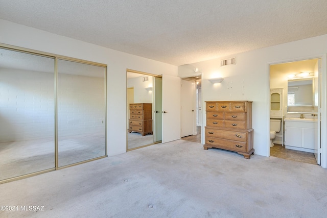 unfurnished bedroom with light colored carpet, a textured ceiling, connected bathroom, and two closets