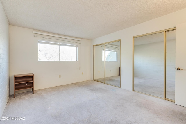 unfurnished bedroom with a textured ceiling, light colored carpet, and multiple closets