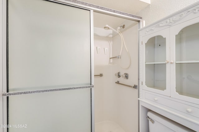 bathroom featuring a shower with door and toilet