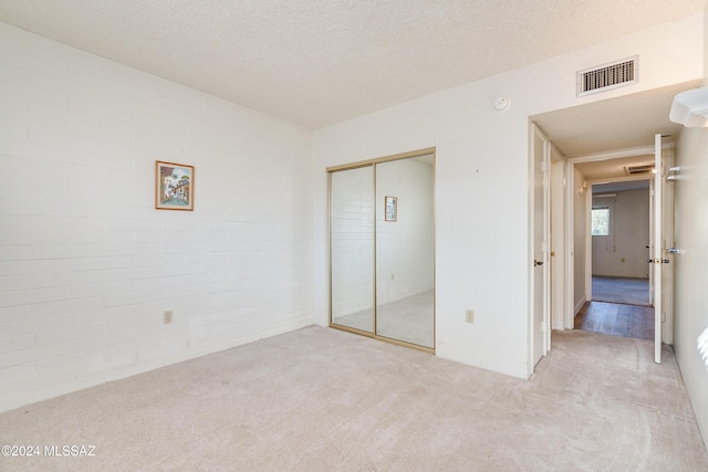 unfurnished bedroom with a textured ceiling, light carpet, and a closet