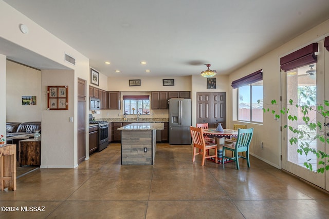 kitchen featuring a wealth of natural light, a center island, dark brown cabinets, and appliances with stainless steel finishes