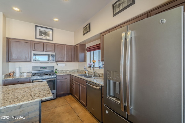 kitchen with sink, light tile patterned floors, dark brown cabinets, light stone counters, and stainless steel appliances