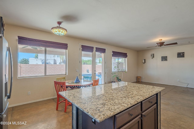 kitchen featuring stainless steel refrigerator with ice dispenser, a center island, light stone counters, and ceiling fan